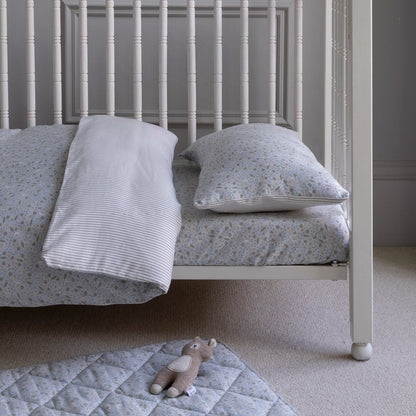 Children's bed with floral bedding and a teddy bear on a quilted mat.