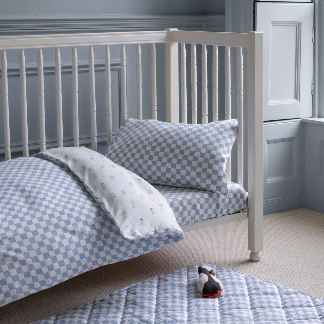 White crib with blue checkered bedding and pillow in a room with gray walls and a white door.