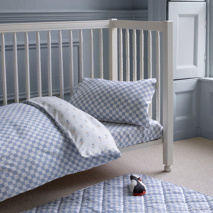 White crib with blue checkered bedding and pillow in a room with gray walls and a white door.