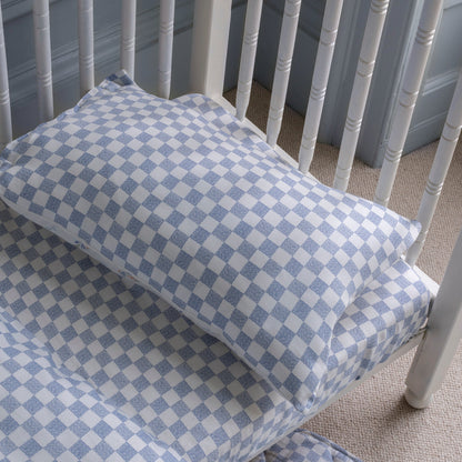 Checkered blue and white crib sheet on a crib with a gray wall in the background