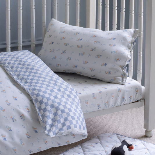 Crib with floral-patterned bedding and checkered blanket against a gray wall.