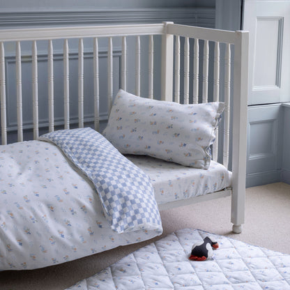 White crib with patterned bedding and pillow in a room with light blue walls.