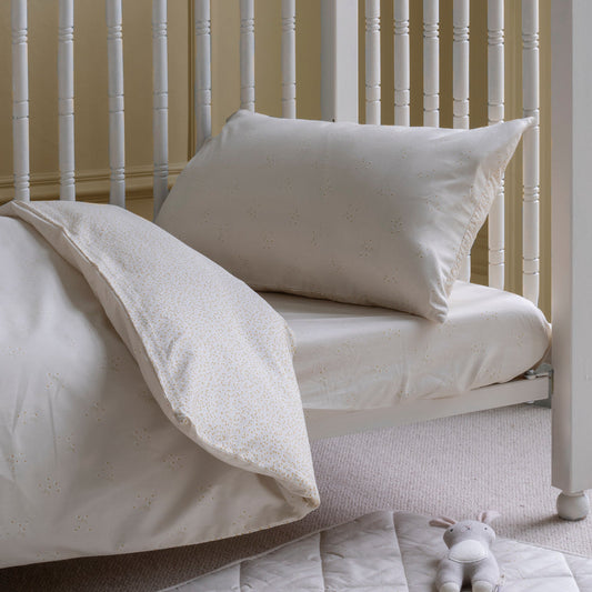 Beige bedding set on a white crib with a plush toy on a light gray blanket.