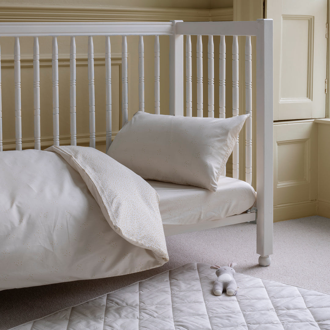 White crib with bedding and a pillow in a neutral-colored room.