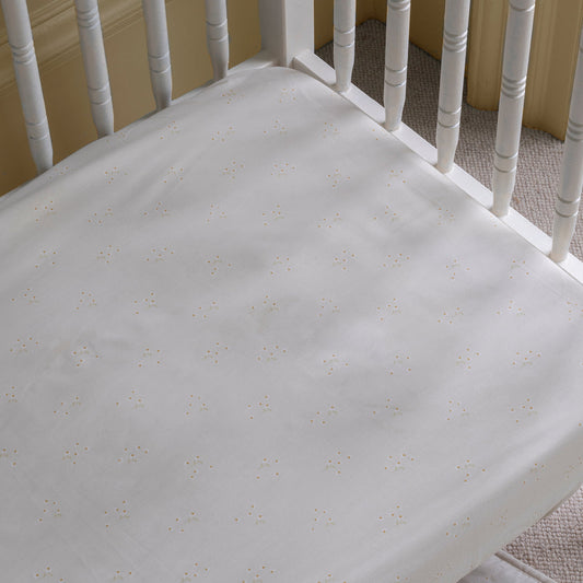 White crib with a textured mattress cover on a carpeted floor.