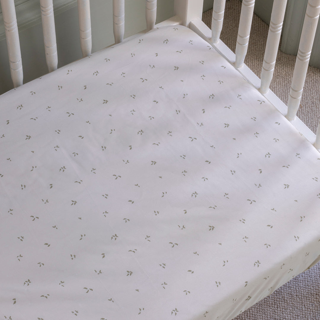 Crib with a fitted sheet featuring a subtle pattern on a carpeted floor.
