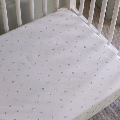 Crib with a fitted sheet featuring a subtle pattern on a carpeted floor.