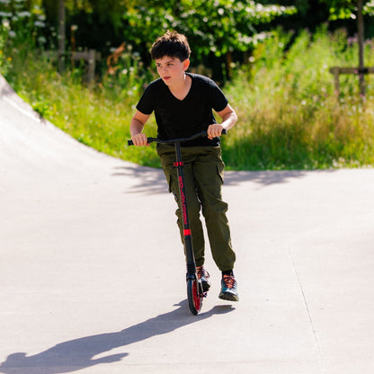 Child riding a scooter on a paved path with greenery in the background