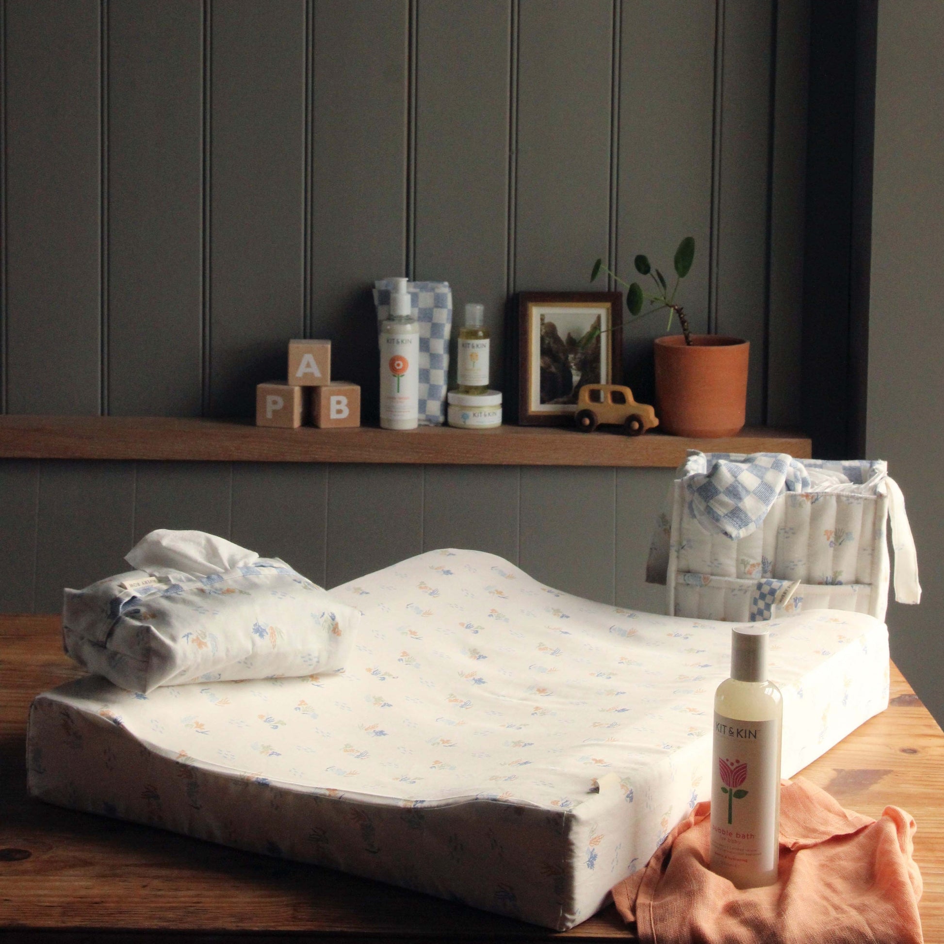 Baby changing table with items on a wooden surface against a dark paneled wall.