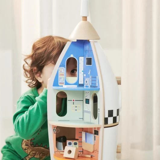 Child peeking out from behind a colorful toy house with a curtain background