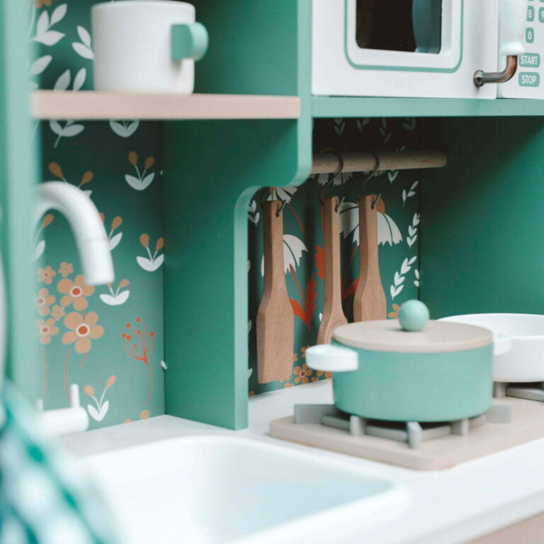 Children's play kitchen set with green stove and white sink against a floral-patterned wall.