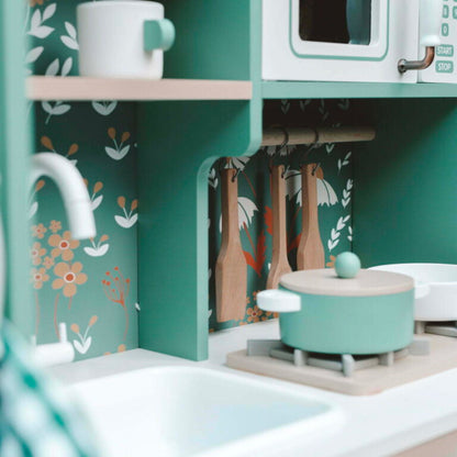 Children's play kitchen set with green stove and white sink against a floral-patterned wall.