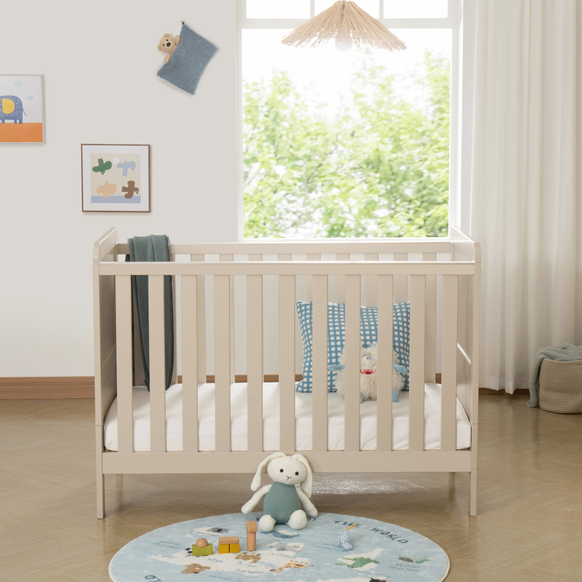 Baby cot in a bright room with toys and a rug on the floor.