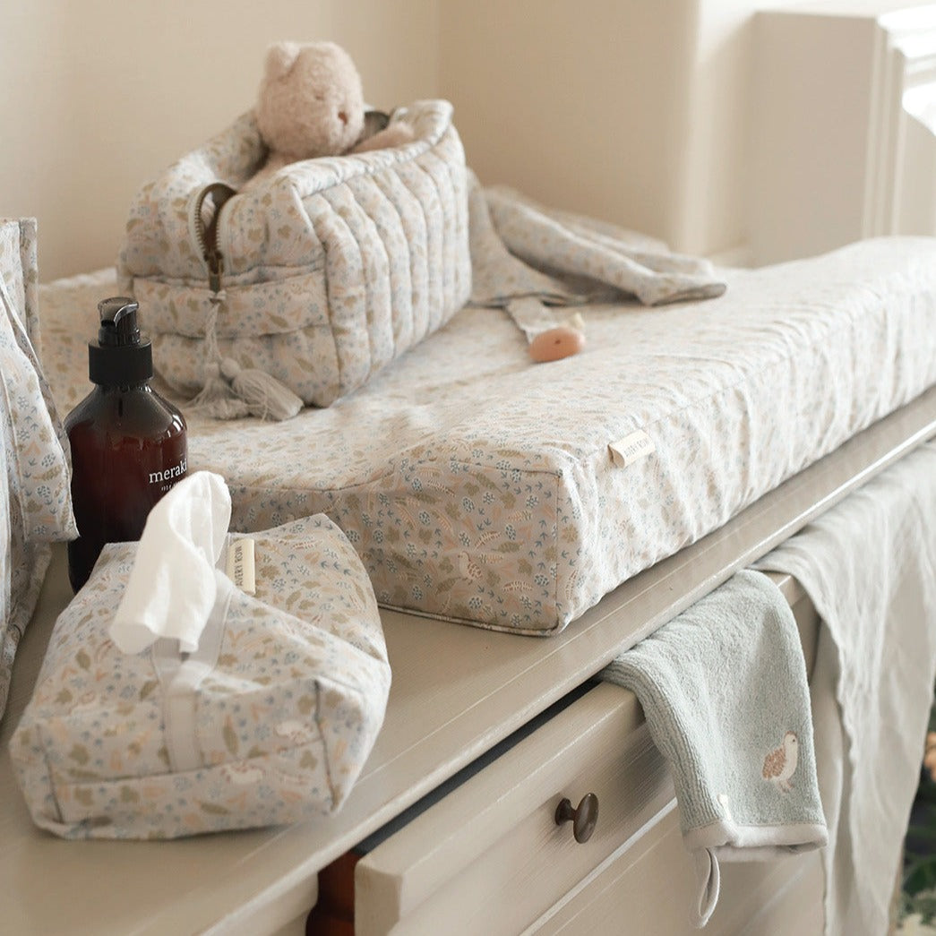 Baby changing table with baby items including a bottle, tissues, and a blanket.