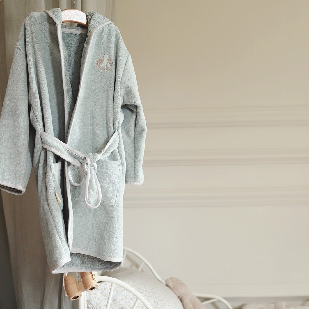 Gray bathrobe with a hood and tie hanging on a wooden hanger against a neutral background.