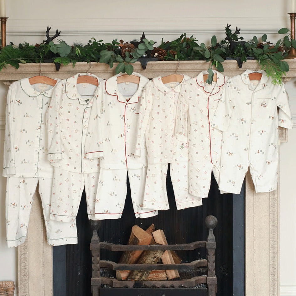 Set of pajama sets hanging on a fireplace mantel with decorative greenery.