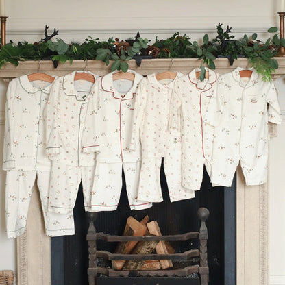 Set of pajama sets hanging on a fireplace mantel with decorative greenery.