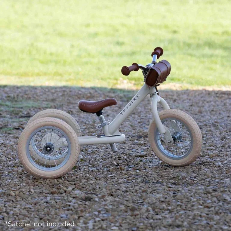 Children's tricycle with brown seat and handlebar on a gravel surface.