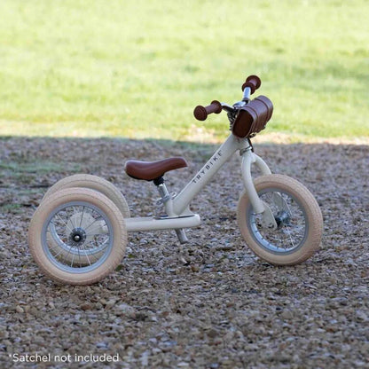 Children's tricycle with brown seat and handlebar on a gravel surface.