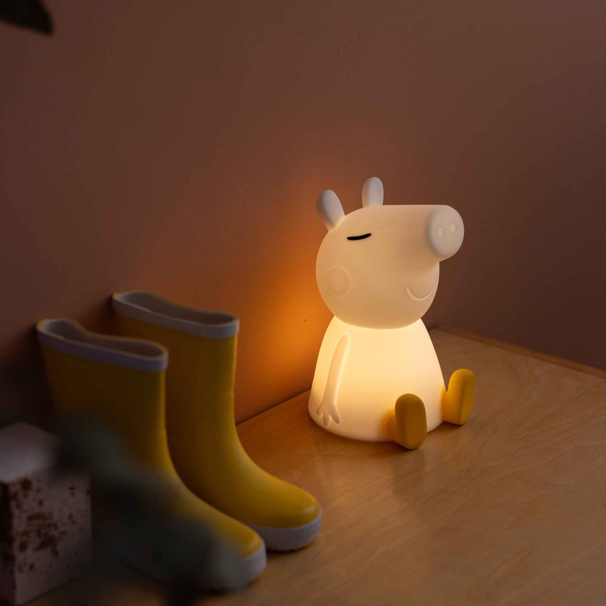 Lampe de chevet en forme d'animal sur une table avec des bottes jaunes et un jouet en bois dans une ambiance chaleureuse.