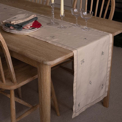 Dining table with a beige table runner, glasses, and plates on a wooden floor.