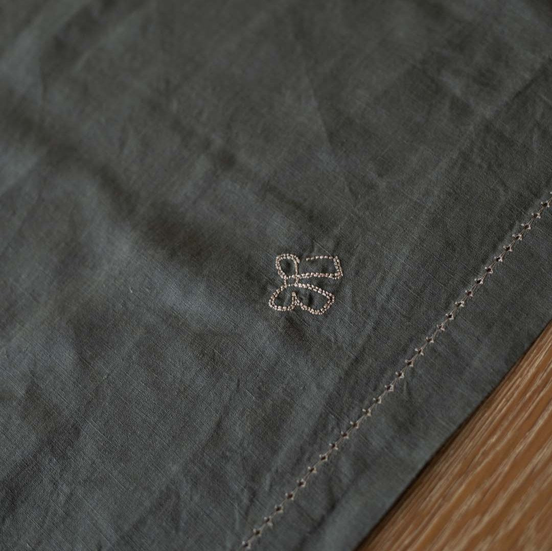 Close-up of a dark fabric with a subtle pattern and a small embroidered design on a wooden surface.
