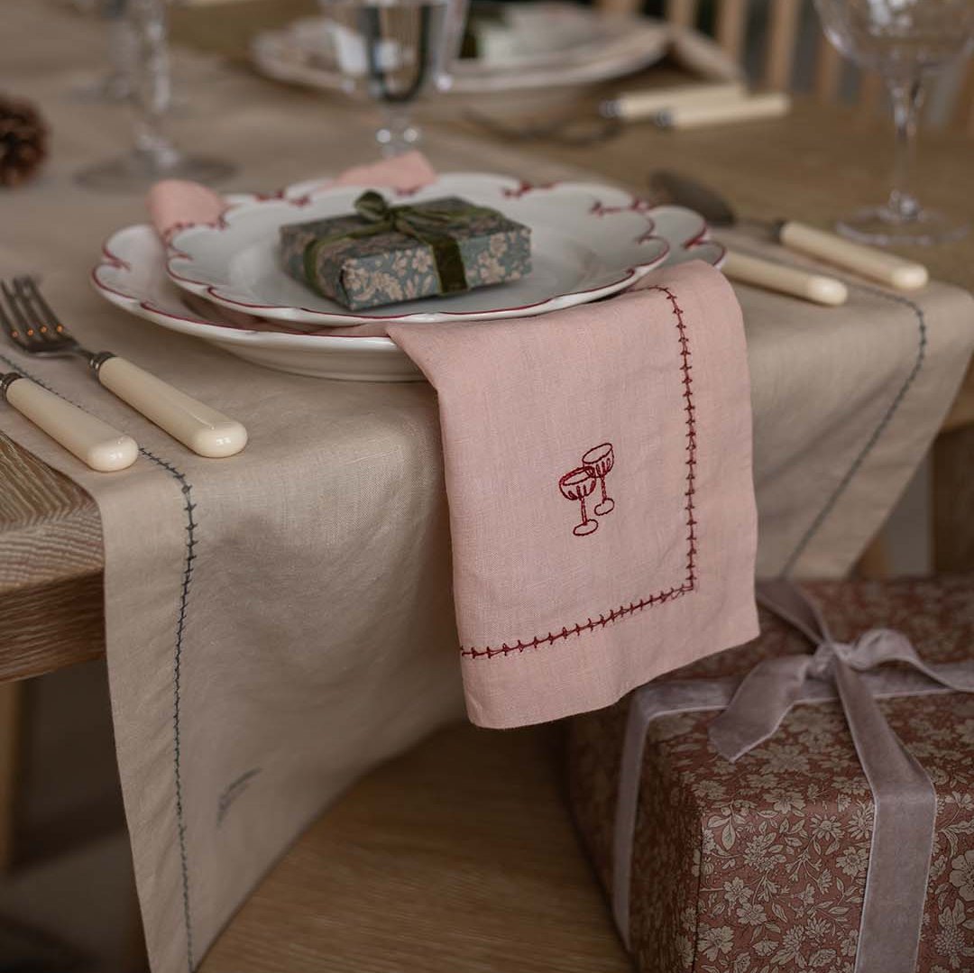 Dining table setting with a pink embroidered napkin, plates, and cutlery.