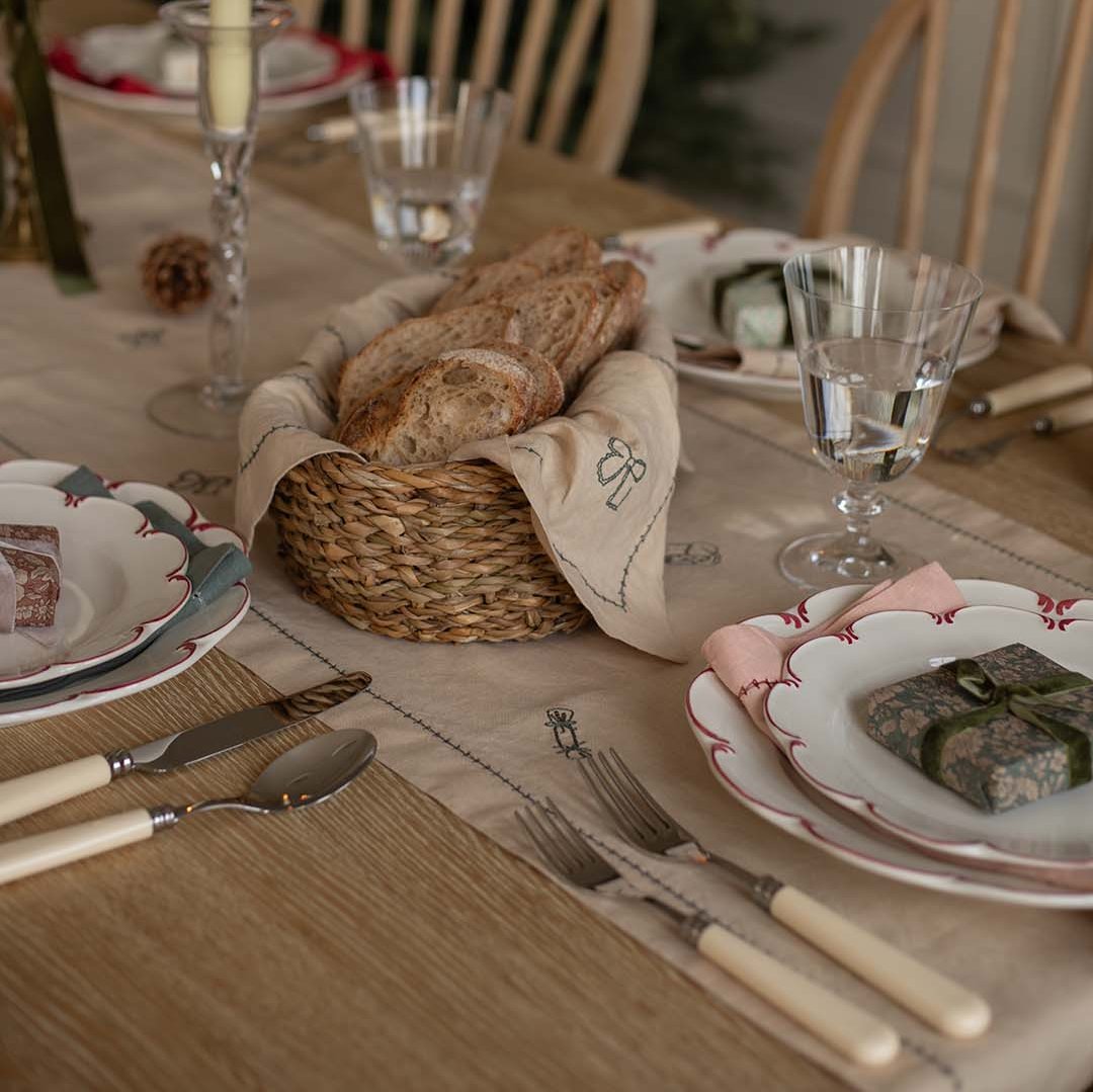 Set dining table with bread basket, plates, and cutlery on a wooden surface.