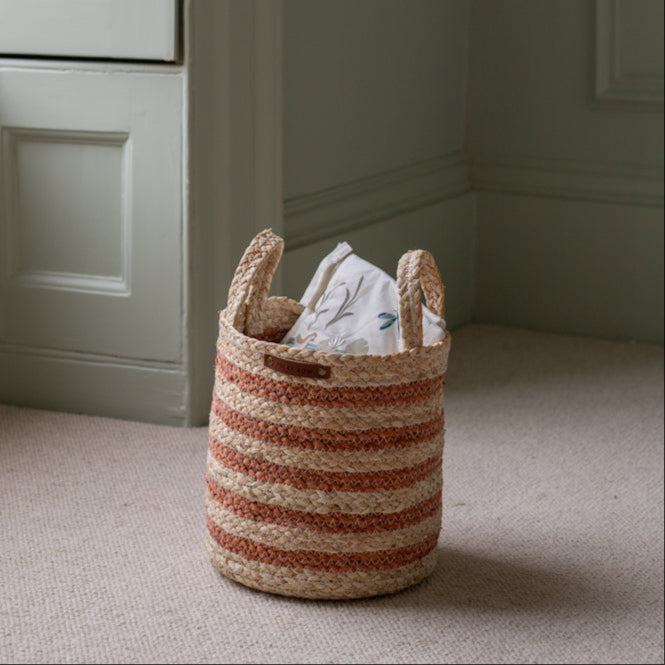 Striped woven basket with a white garment on a carpeted floor against a neutral wall.