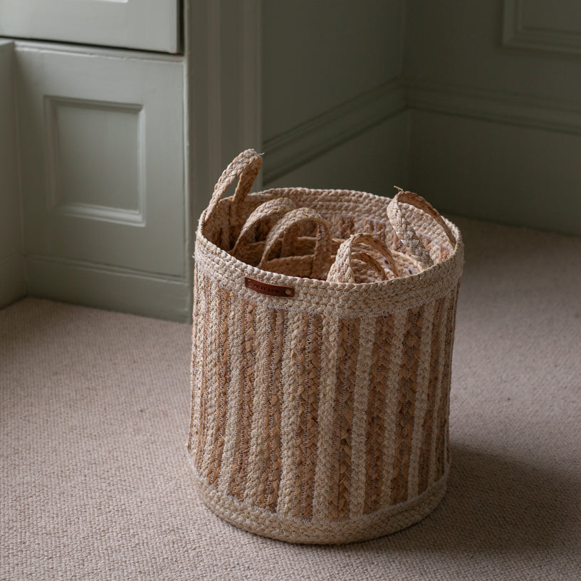 Woven basket with handles on a carpeted floor against a neutral wall.
