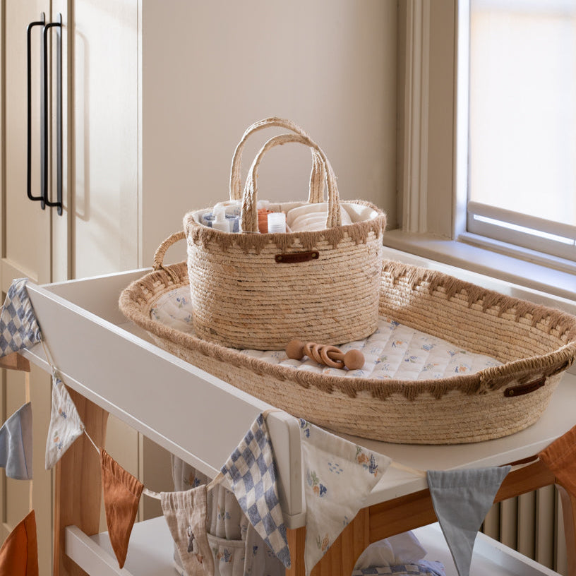 Wicker crib and basket on a white dresser with a window in the background
