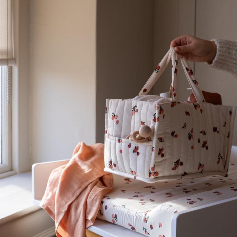 Floral-patterned baby bag held by a hand on a light-colored surface with a window in the background