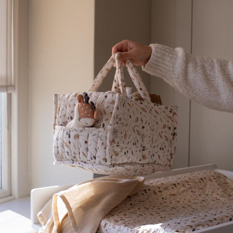 Person holding a patterned baby basket with toys inside, placed on a changing table.
