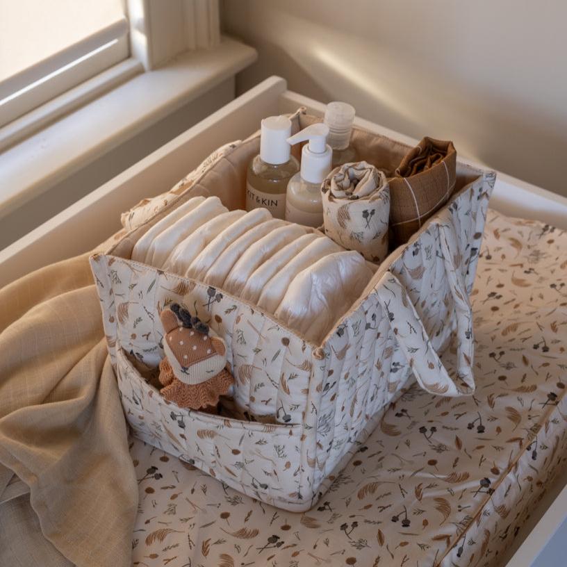 Storage basket with baby items including bottles and diapers on a bed.