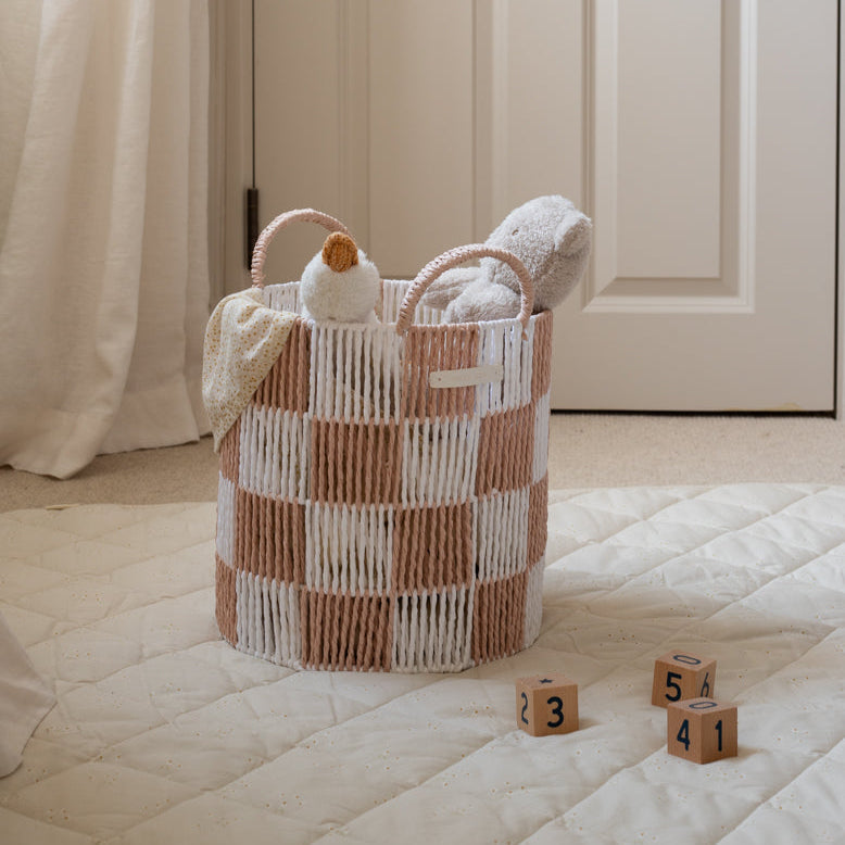 Woven basket with towels and a duck toy on a bed, with wooden blocks in the foreground.
