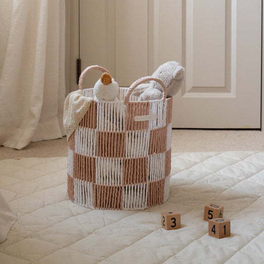 Woven basket with towels and a duck toy on a bed, with wooden blocks in the foreground.