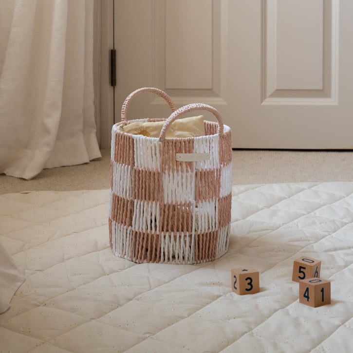 Woven basket with checkered pattern on a bed with wooden blocks displaying numbers.