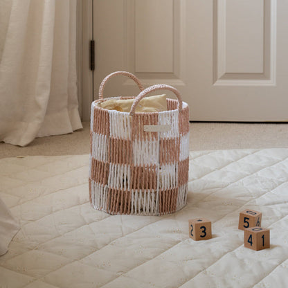 Woven basket with checkered pattern on a bed with wooden blocks displaying numbers.