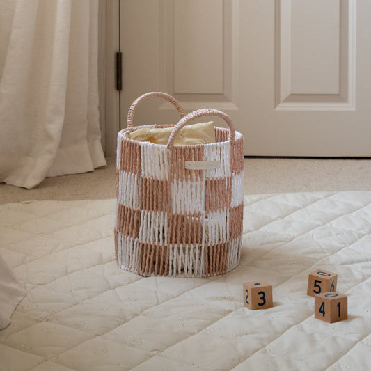 Woven basket with checkered pattern on a bed with wooden blocks displaying numbers.