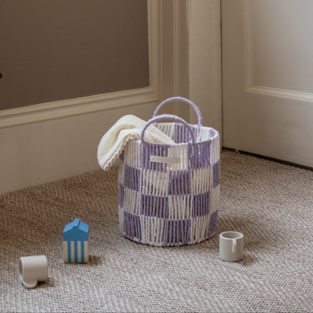 Checkered woven basket with a towel on a textured floor next to children's toys.