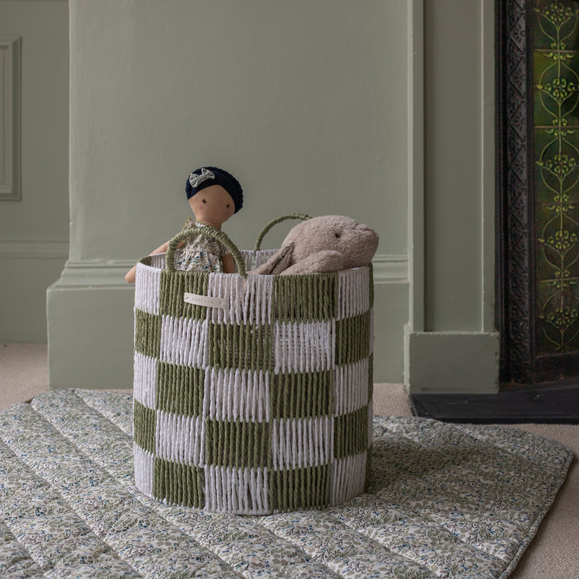 Green and white checkered basket with toys inside, placed on a patterned rug.