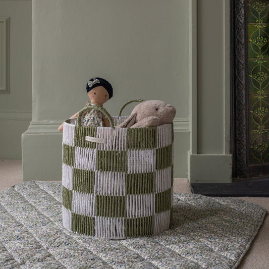 Green and white checkered basket with toys inside, placed on a patterned rug.