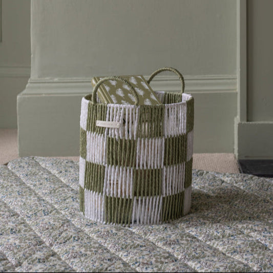 Woven basket with green and white checkered pattern on a textured surface.
