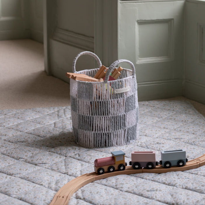 Toy train on a wooden track next to a woven basket on a carpeted floor.