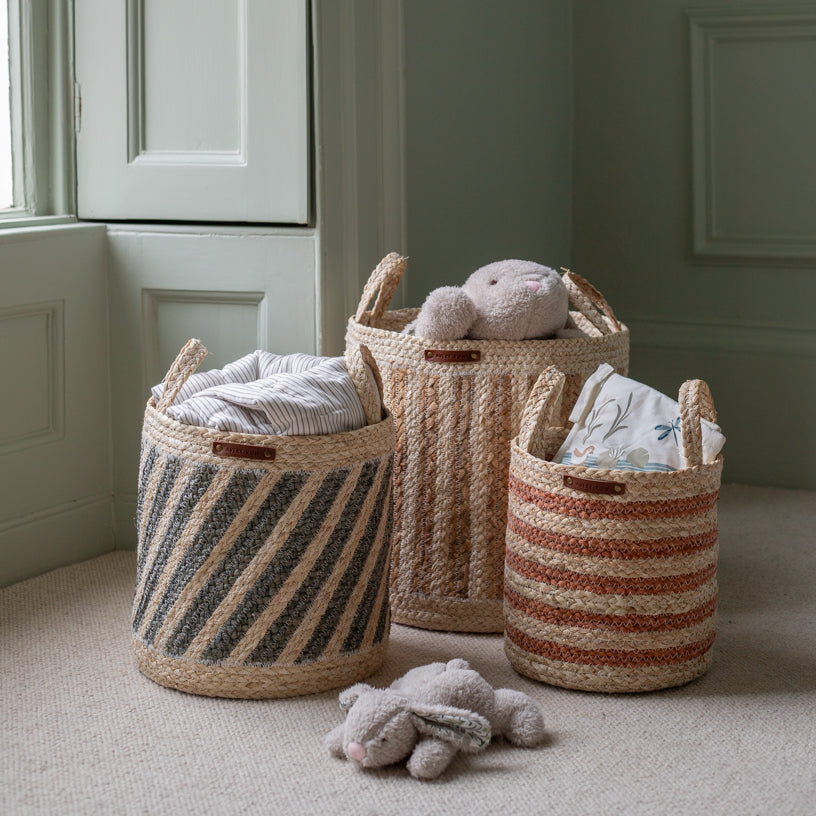 Three woven baskets with striped patterns on a carpeted floor.