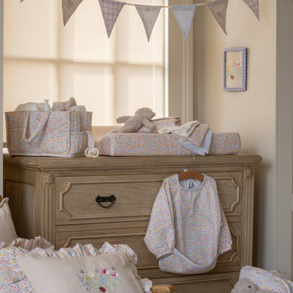 Nursery room with wooden dresser, baby clothes, and toys.