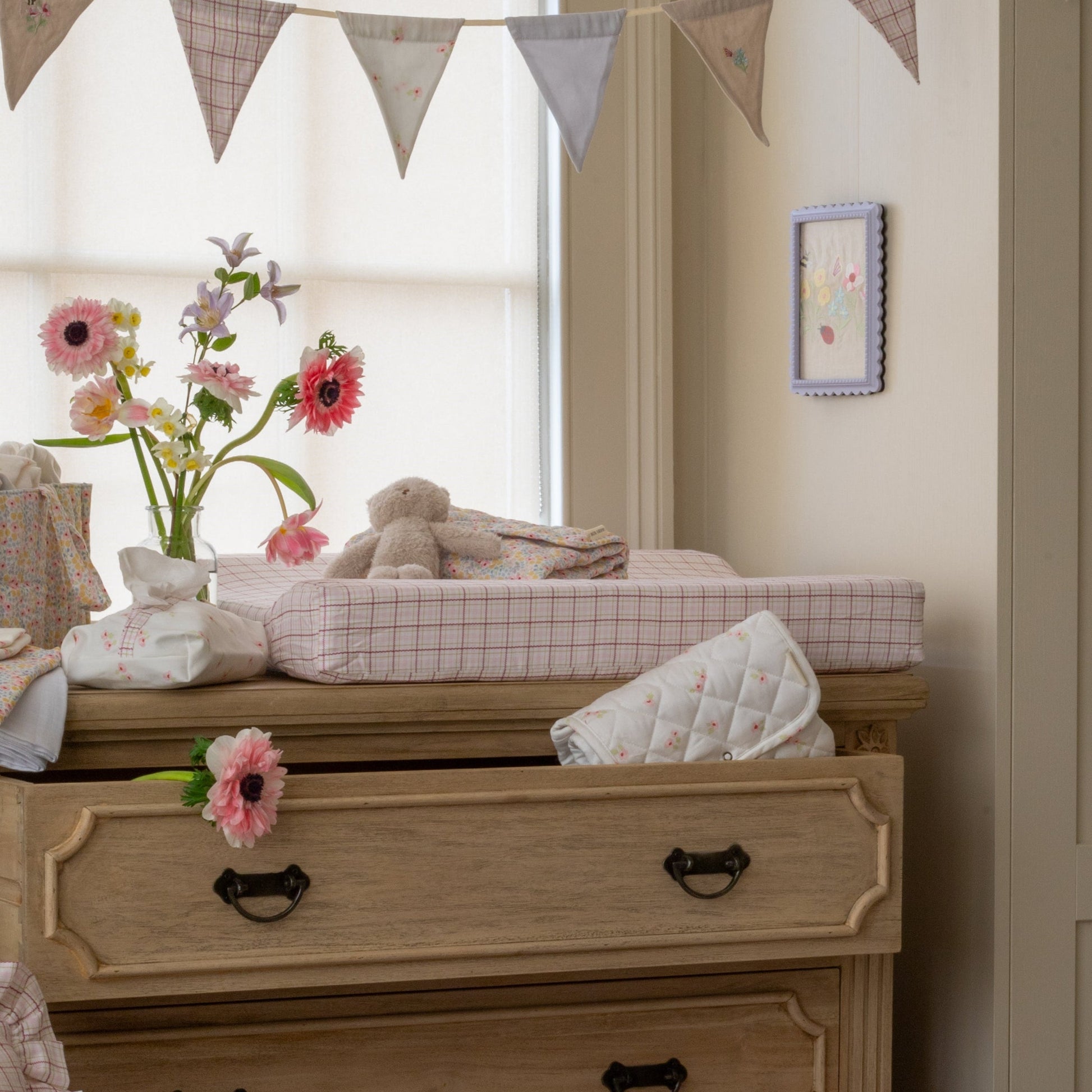 Nursery room with wooden dresser, flowers, and toys.
