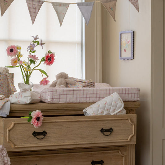 Nursery room with wooden dresser, flowers, and toys.