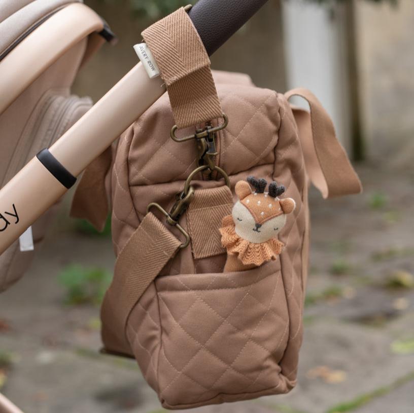 Brown quilted bag attached to a stroller with a small deer plush toy on a blurred outdoor background