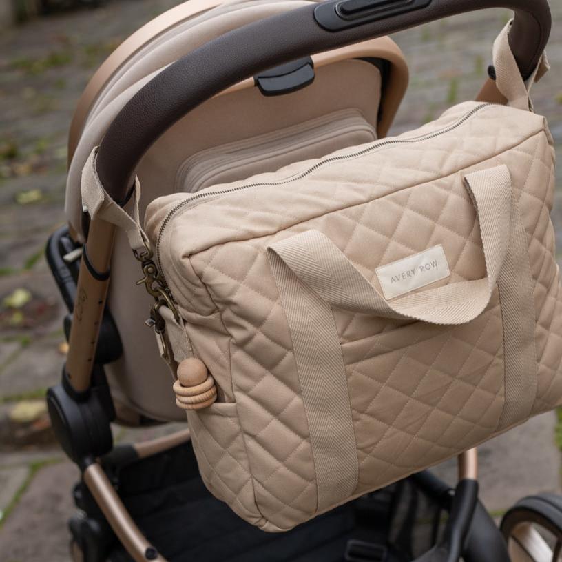 Beige quilted baby bag attached to a stroller with a blurred outdoor background